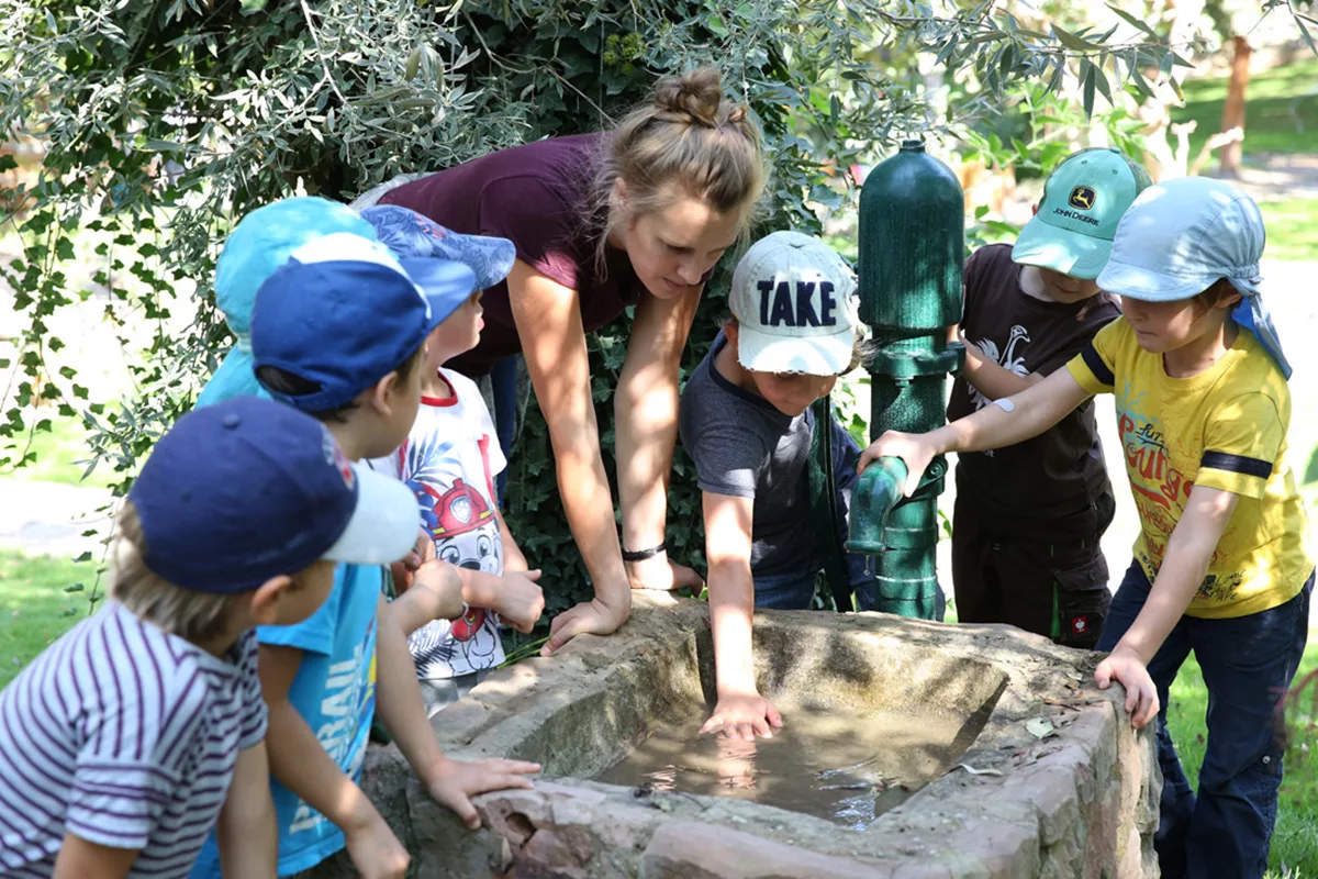 Erzieherin mit Kindergartenkindern am Brunnen